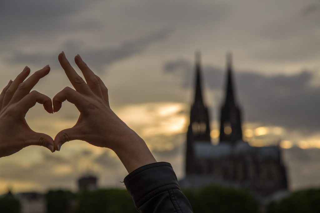 Eine Hand formt ein Herz, im Hintergrund der Kölner Dom